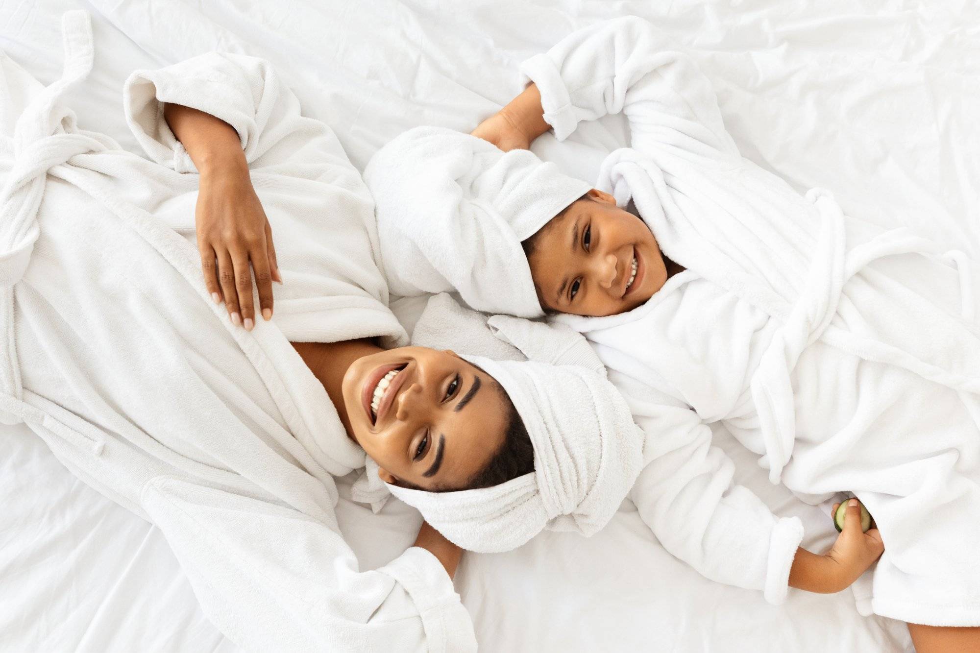 Happy African Mother And Daughter In Bathrobes And Towels Lying On Bed Happy African Mother And Daughter In Bathrobes And Towels Lying On Bed